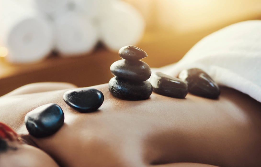 A woman lying on her front receiving hot stone treatment on her back