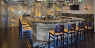 Top bar shelf filled with alcohol above the bar counter and chairs