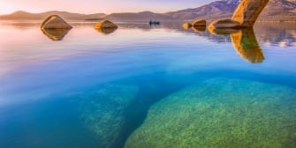 Rock formations on the water next to towering mountains during a sunset