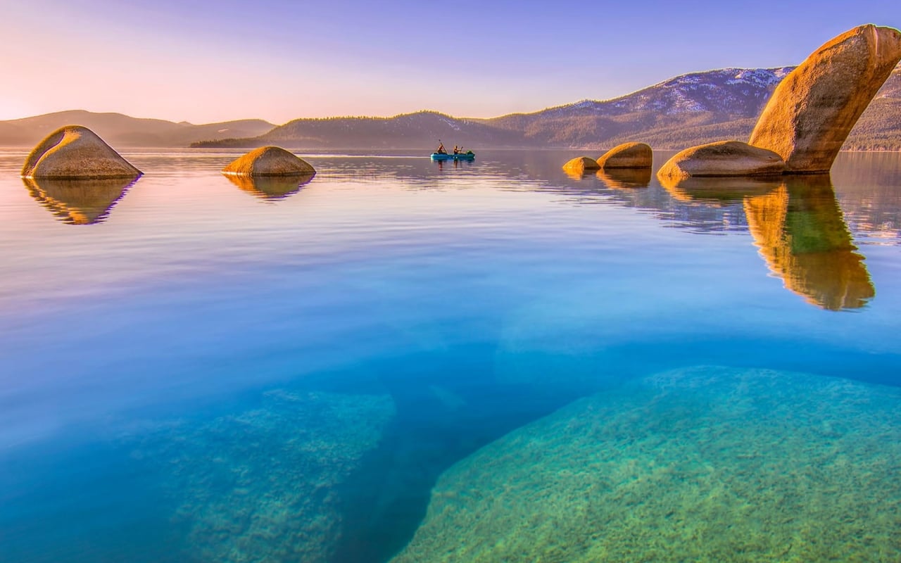 A serene lake scene with large rocks, a mountain backdrop, and a couple in a boat.