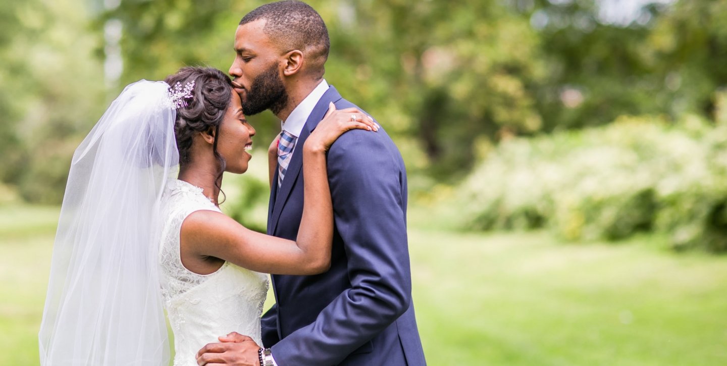 The groom kissing the bride's forehead in the outdoors