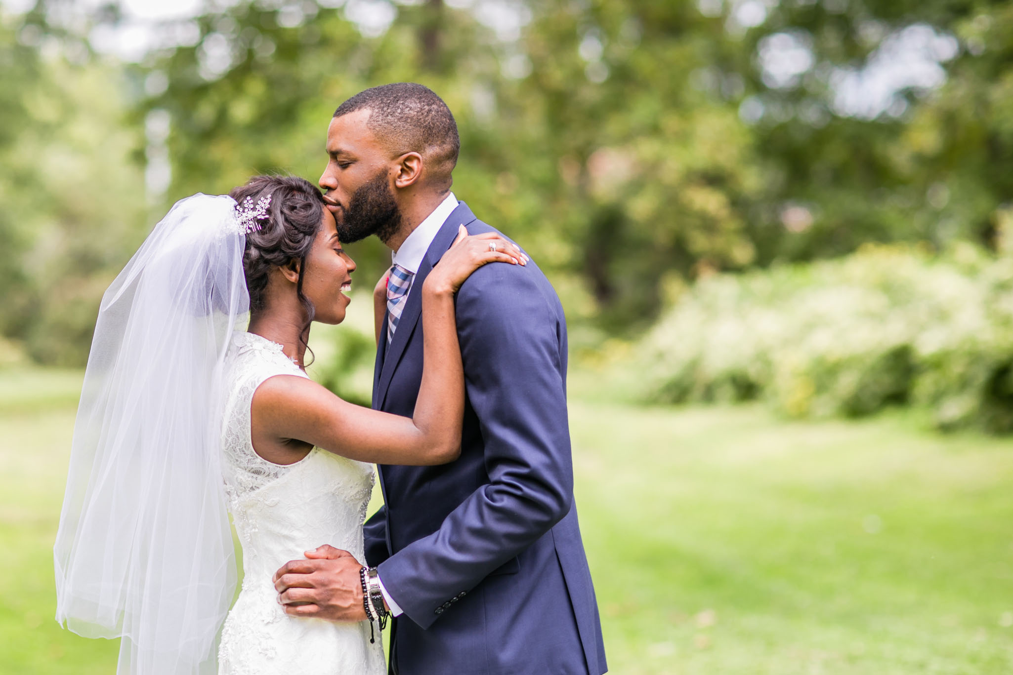 The groom kissing the bride's forehead in the outdoors