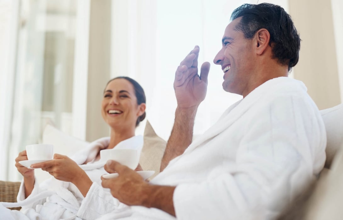 A couple wearing robes drinking coffee while sitting on the sofa