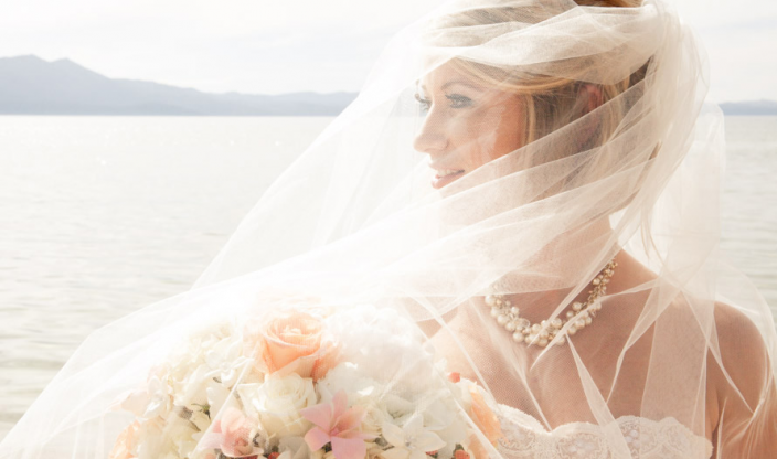 A bride with a tulle veil covering her face holding a flower bouquet