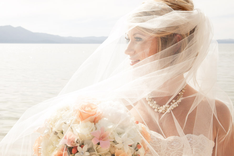 A bride with a tulle veil covering her face holding a flower bouquet