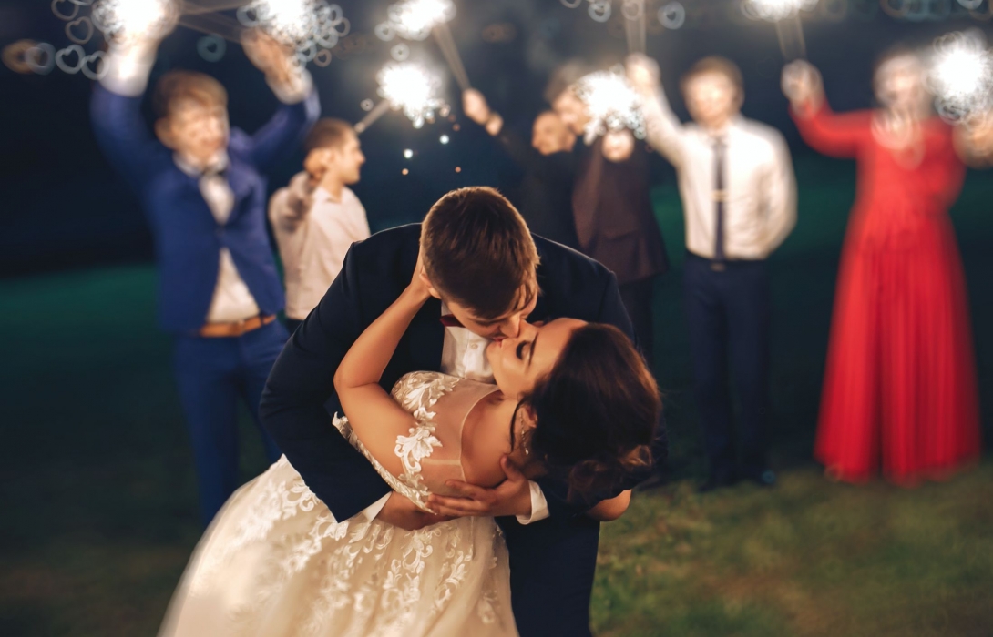Groom kissing the bride with blurred image of guests holding sparklers in the background