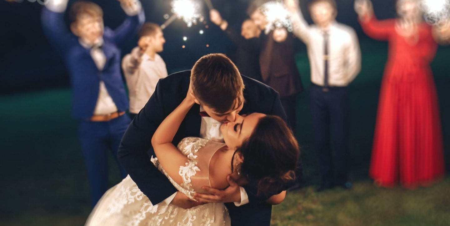 Groom kissing the bride with blurred image of guests holding sparklers in the background