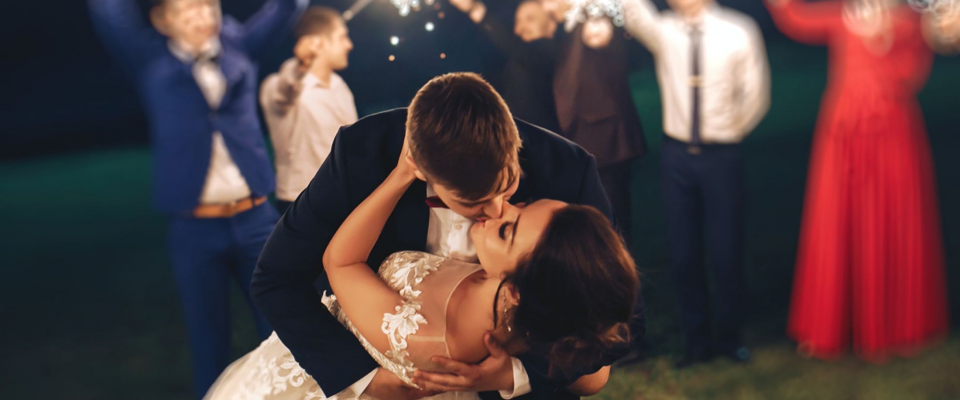 Groom kissing the bride with blurred image of guests holding sparklers in the background