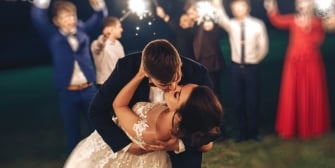 Groom kissing the bride with blurred image of guests holding sparklers in the background