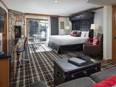 A spacious bed with a wooden headboard overlooking an accent stone wall and a TV above the dresser
