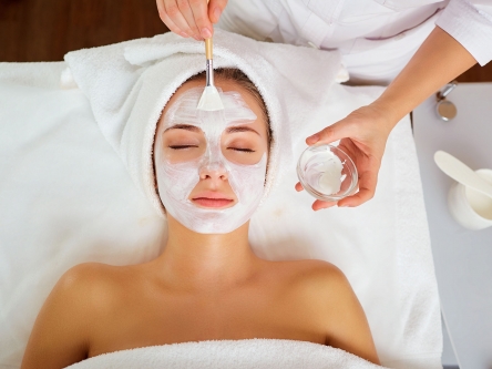 An aesthetician's hand applying a white facial mask on a woman's face