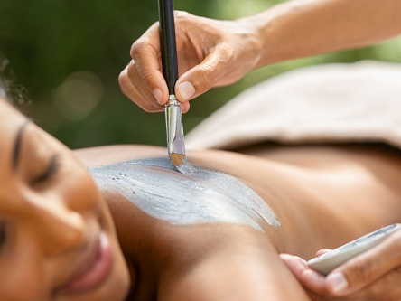 A woman receiving a mud spa treatment on her back from the hands of the therapist