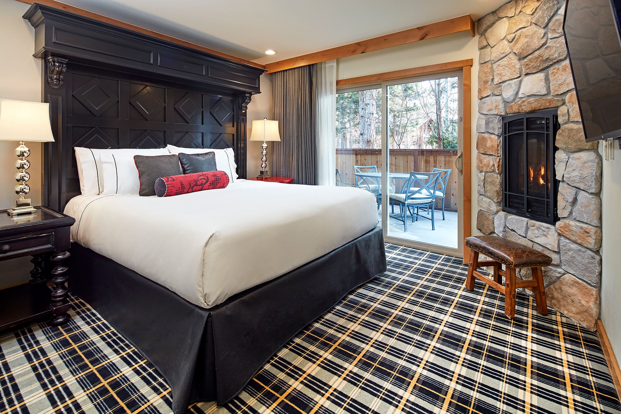 A hotel room with a large bed, stone fireplace, and sliding glass door to a balcony