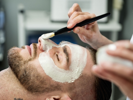 An aesthetician is applying a facial mask on a man at the spa.