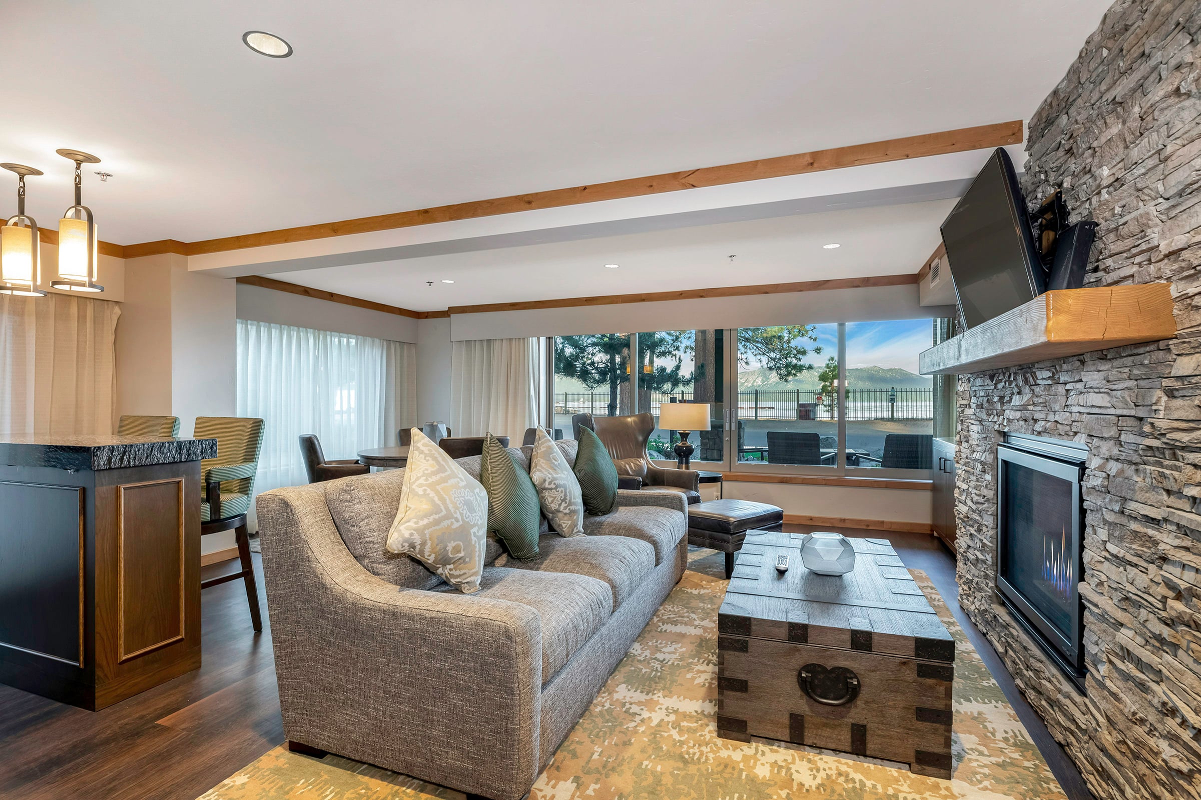 A wide view of a living room with a gray sofa, stone fireplace, and large windows.