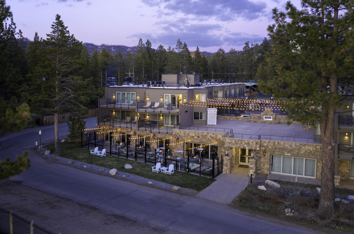 A multi-story building with a stone facade and balconies, surrounded by trees and a road.