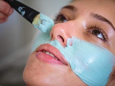 A close up of an aesthetician's hand applying a blue face mask on a woman