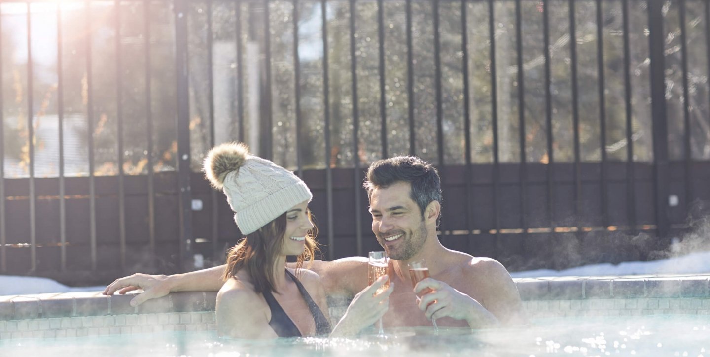 A woman and man clinking their champagne flutes while soaking in the hot tub