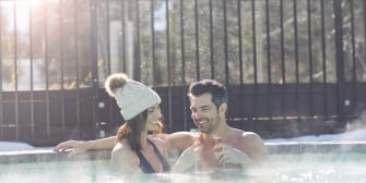 A woman and man clinking their champagne flutes while soaking in the hot tub