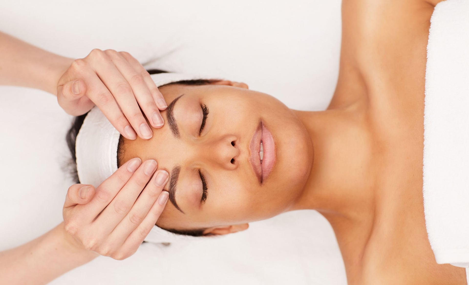 A woman receiving a forehead massage from the hands of an aesthetician
