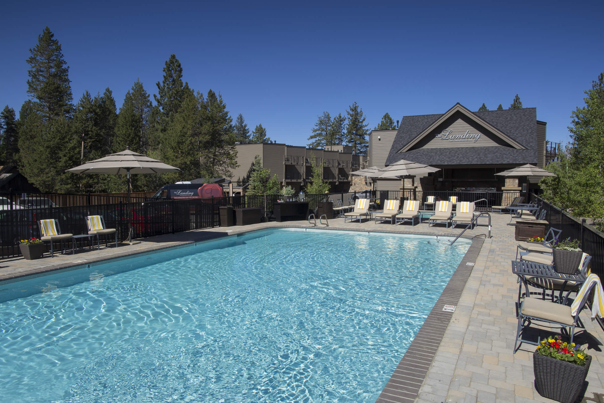 A swimming pool with lounge chairs and umbrellas, surrounded by a building and trees.