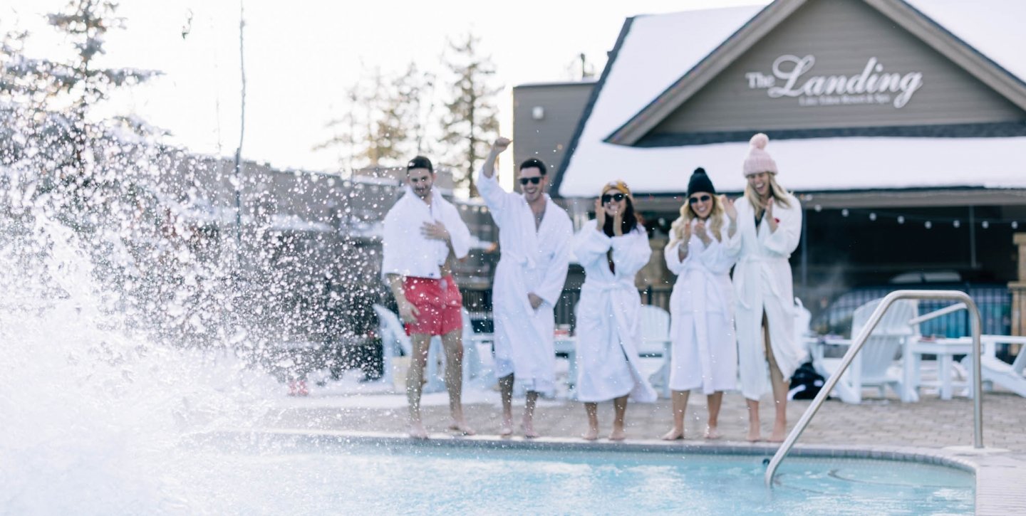 Group of friends laughing by the pool in robes