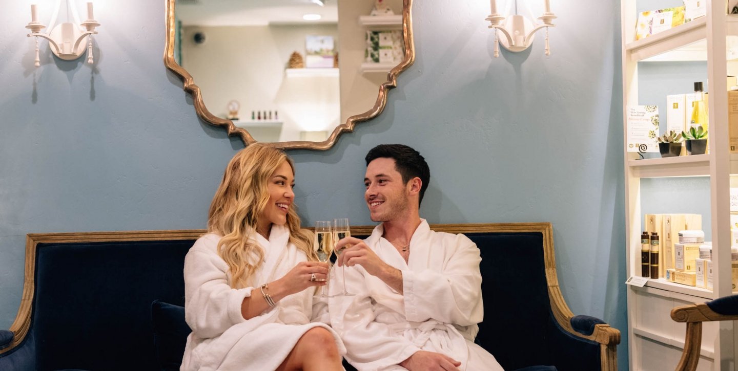Couple clinking champagne glasses in robes at the spa