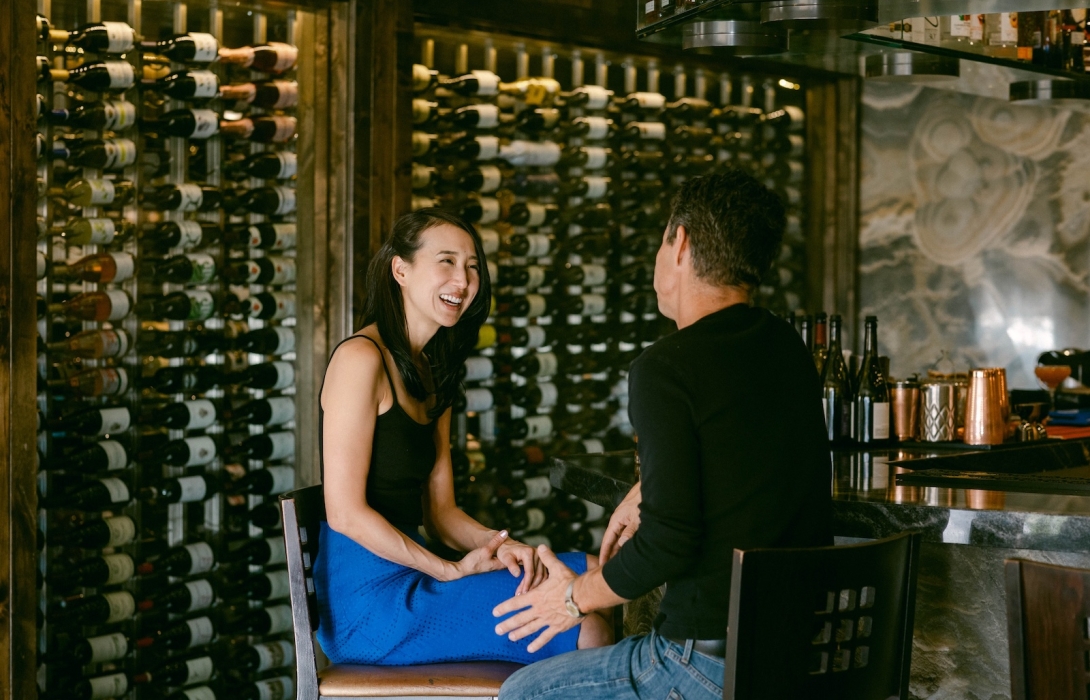 Couple laughing on a date with wine bottles in the back