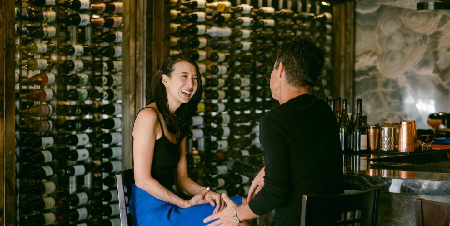 Couple laughing on a date with wine bottles in the back