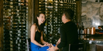 Couple laughing on a date with wine bottles in the back