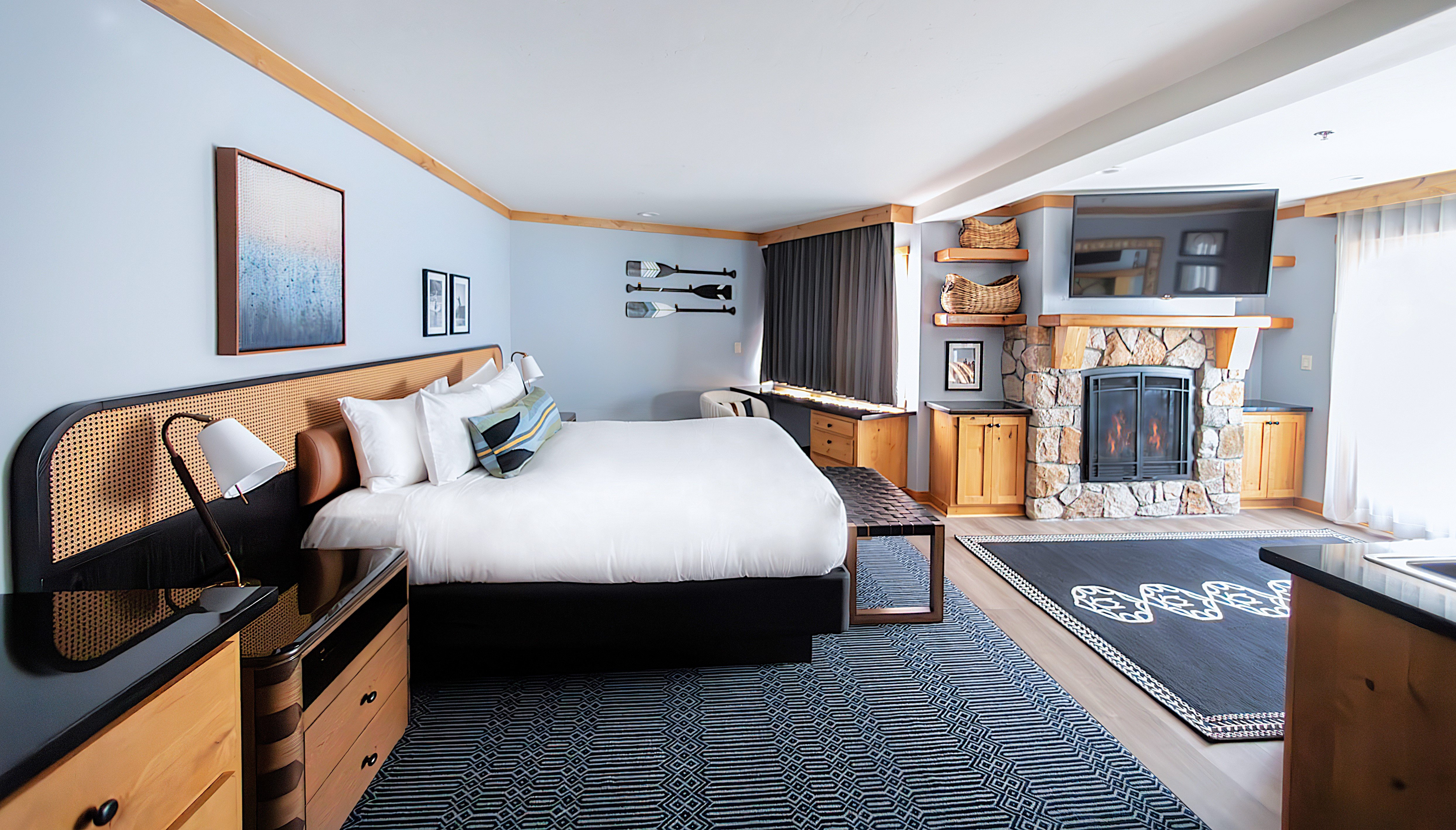 A wide shot of a hotel room with a bed, fireplace, and TV