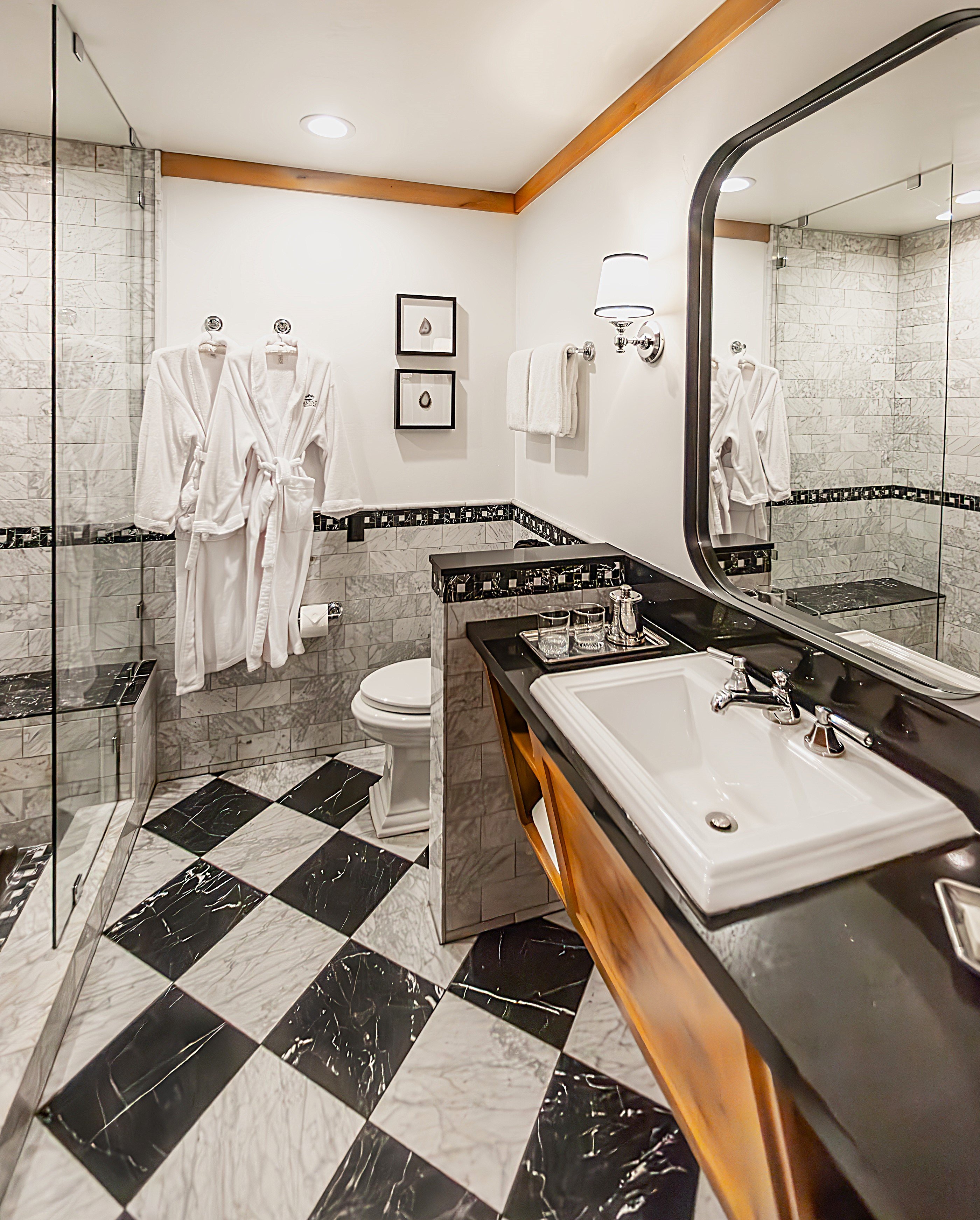 A bathroom with a black and white checkered floor, a shower with a glass door, a toilet, and a sink with a black countertop.