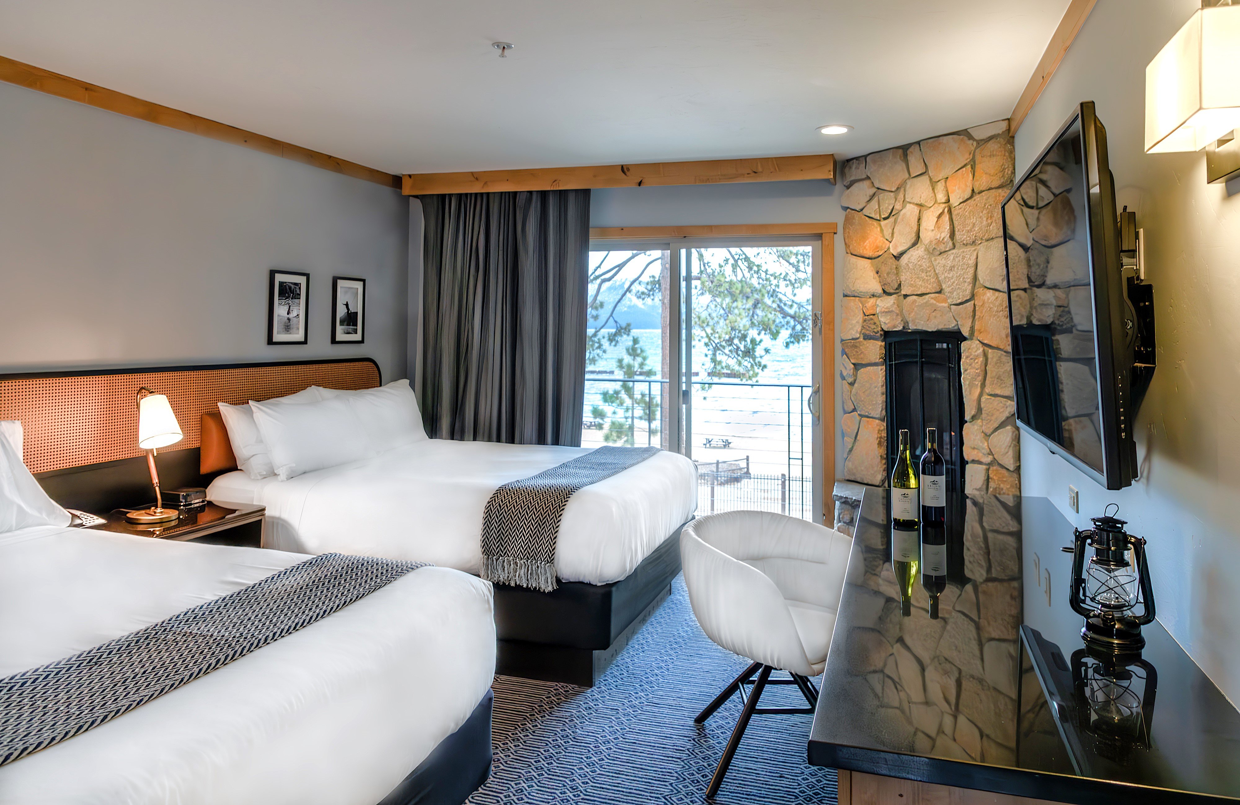 A hotel room with two beds, a stone fireplace, and a balcony with a view.
