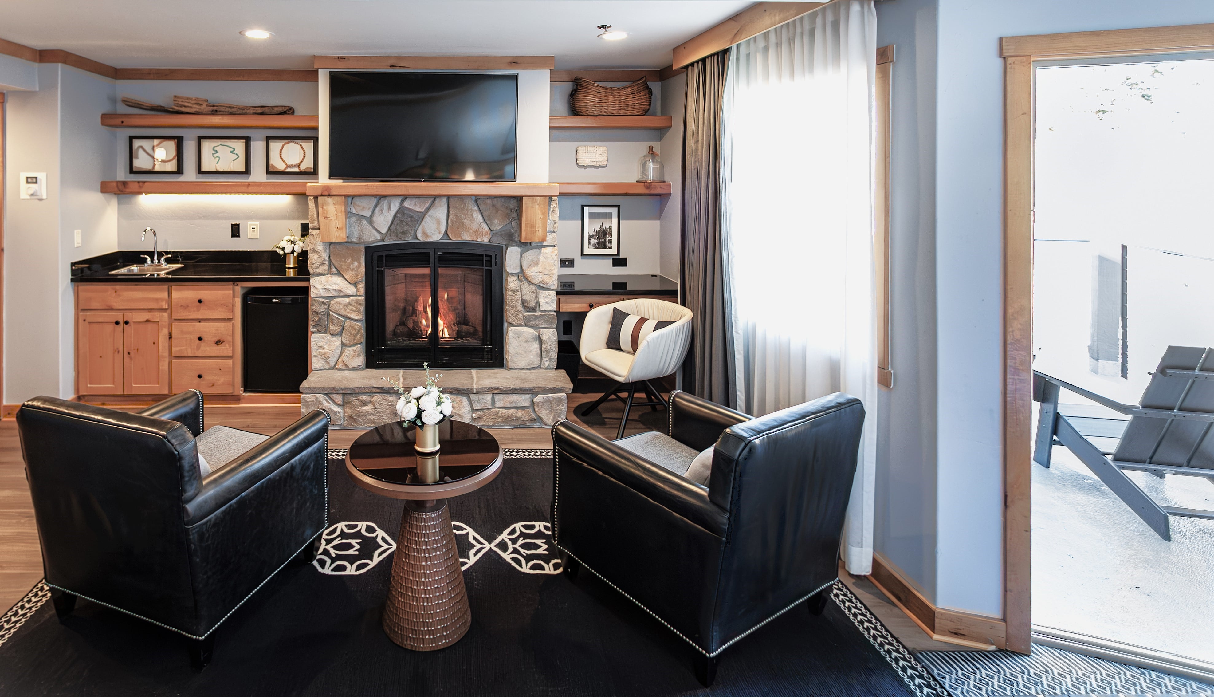 A cozy living room with a fireplace, kitchenette, and seating area.