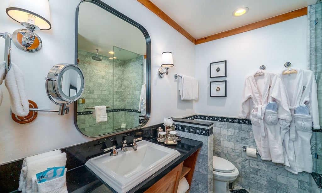 A clean and luxurious bathroom with marble tiles, a glass-enclosed shower, and plush robes.