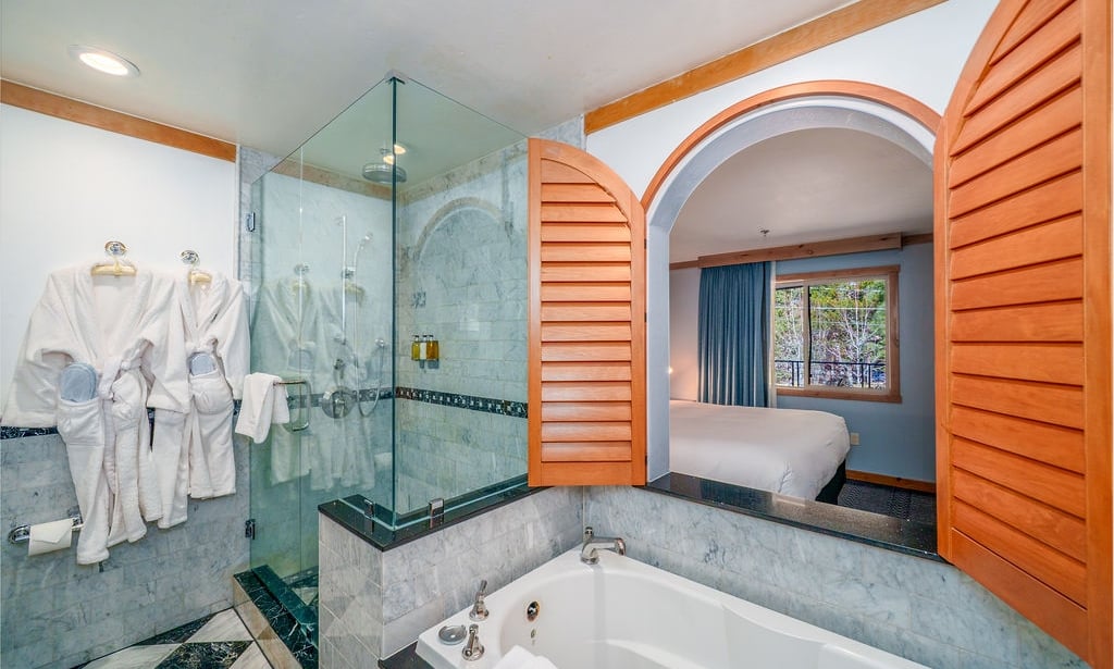 A bathroom with a large bathtub, shower, and robes hanging on the wall.