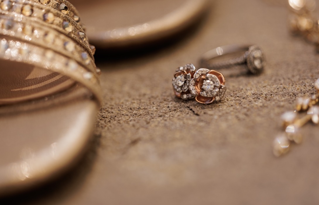 Close-up of diamond rings and a jeweled bracelet on a sandy surface with warm lighting.