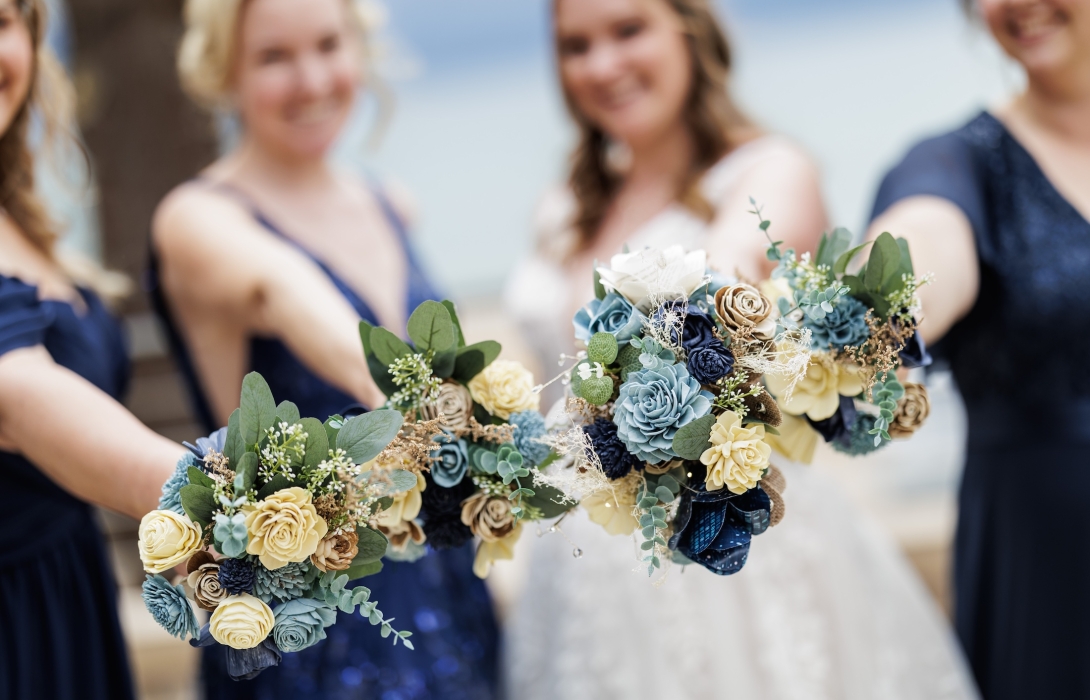 Close-up of matching blue, cream, and green floral bouquets held by bridesmaids in navy dresses with a blurred wedding party background.