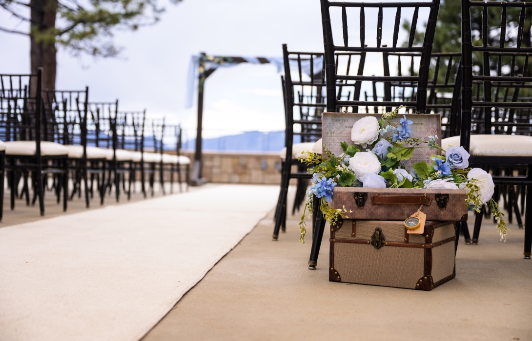 Outdoor wedding setup with black Chiavari chairs and a vintage suitcase overflowing with white and blue flowers at the aisle.