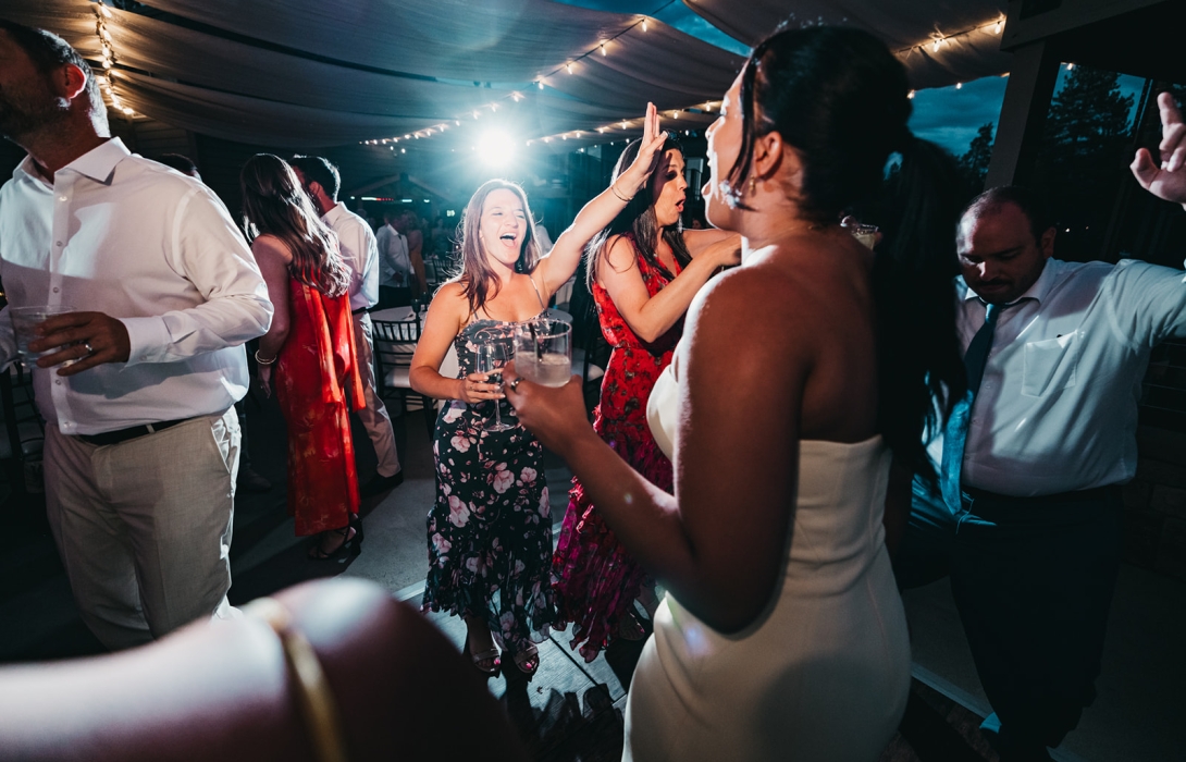 Group of guests dancing at a nighttime party under string lights, holding drinks and enjoying the music.