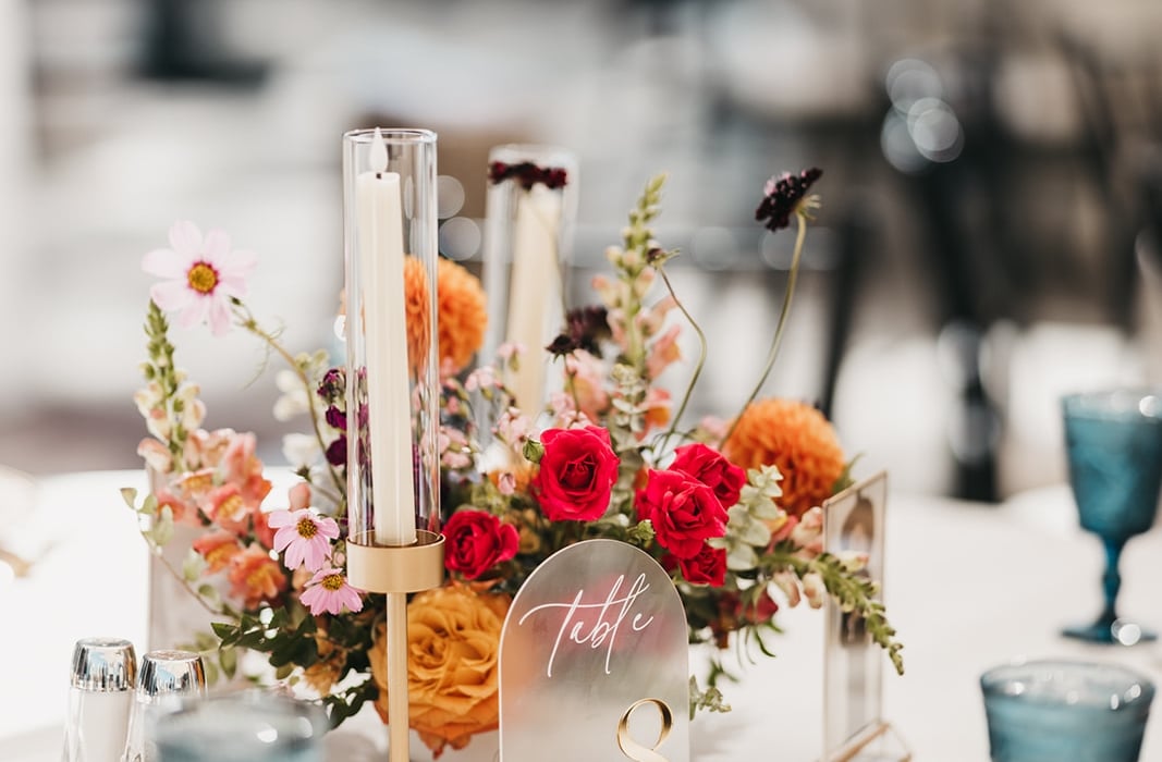 Table centerpiece with pink, orange, and red flowers in a glass vase, candle holders, and a 'Table 8' card.