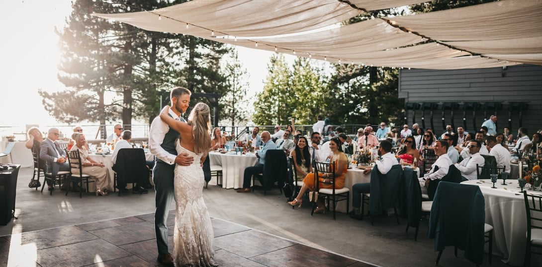 A wedding reception with a bride and groom dancing under a white fabric canopy, surrounded by seated guests at tables.